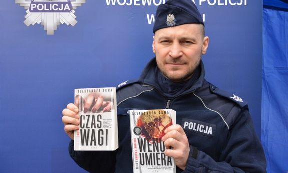 Umundurowany policjant  trzyma dwie książki w ręku