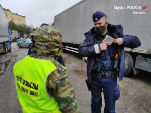 Policjant i Strażnik Graniczny na tle radiowozów policyjnych