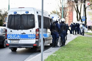 Policyjny radiowóz i policjanci zabezpieczający rejon stadionu miejskiego.&quot;&gt;