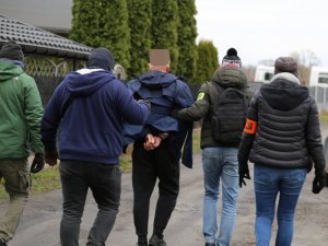 grupa nieumundurowanych policjantów prowadzi zatrzymanego mężczyznę