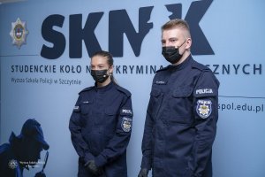 policjant i policjantka stoją na tle ściany