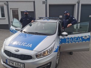 dwaj policjanci stoją przy radiowozie