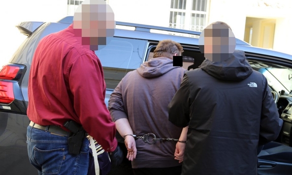 dwaj nieumundurowani policjanci prowadzą zatrzymanego do radiowozu policyjnego