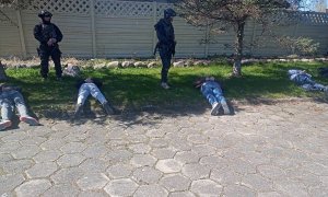 czterej zatrzymali leżą skuci w kajdankach na trawie, nad nimi stoją dwaj policjanci