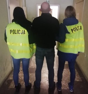 Policjantki prowadzą podejrzanego o kradzież korytarzem w jednostce Policji