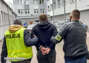 Nieumundurowani policjanci przeprowadzają zatrzymanego mężczyznę do radiowozu