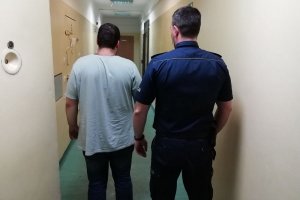 policjant prowadzi korytarzem zatrzymanego mężczyznę