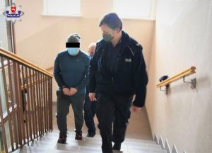 zatrzymany mężczyzna w kajdankach idzie po schodach obok policjanci