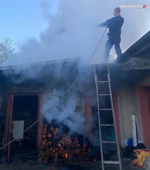 Policjant stojąc na dachu budynku gasi pożar