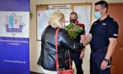 Dwaj umundurowani policjanci i kobieta, która w ręku trzyma kwiaty