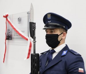Policjant z bagnetem, z tyłu widoczna tablica z biało - czerwoną szarfą