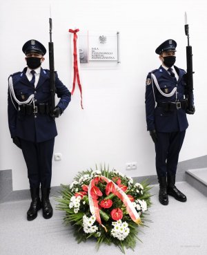 dwaj umundurowani policjanci z bagnetami na ramieniu stoją po obu stronach tablicy z napisem: Sala konferencyjna im. Państwowego Korpusu Bezpieczeństwa, na dole, pod tablica wieniec z kwiatów