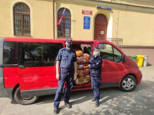 policjantka i policjant stoją obok busa z otwartymi drzwiami, przez które widać worki z nakrętkami