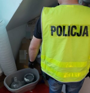 Mężczyzna w kamizelce z napisem policja stoi w mieszkaniu przy pakunkach.&quot;&gt;