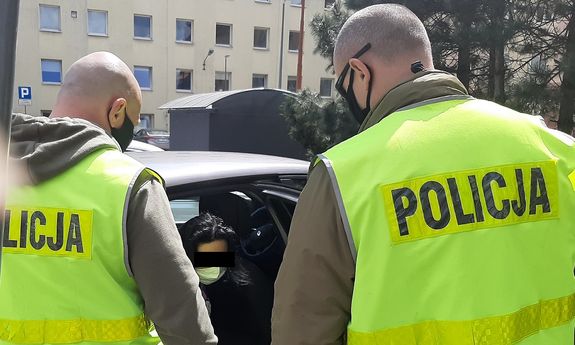 Dwaj policjanci w żółtych kamizelkach z napisem Policja podczas konwojowania zatrzymanej