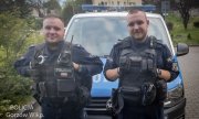 dwaj umundurowani policjanci stoją przed radiowozem
