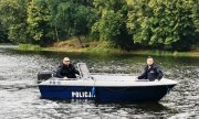 dwaj umundurowani funkcjonariusze płyną łodzią służbową po rzece