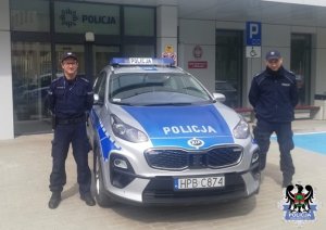 dwaj umundurowani policjanci stojący przy radiowozie