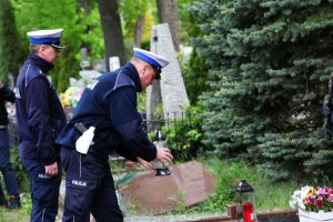 Dwaj policjanci przy grobie. Jeden z nich stawia na nim znicz