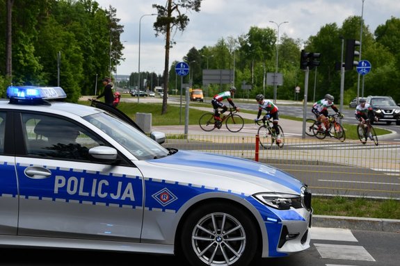 na pierwszym planie policyjny radiowóz. w tle kolarze przygotowujący się do startu