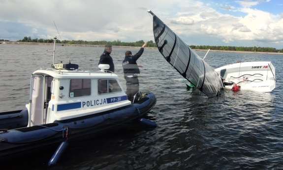 Policyjna łódka na które stoi dwóch policjantów, jeden z nich trzyma żaglówkę