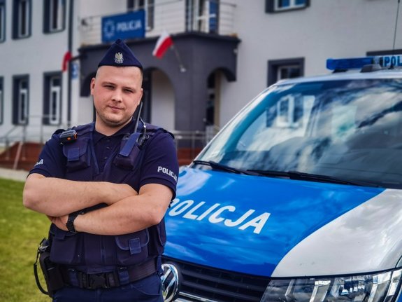 policjant stoi przy radiowozie, w tle budynek komendy