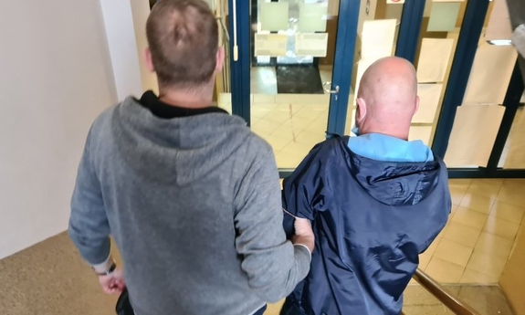 policjant prowadzi po schodach zatrzymanego mężczyznę