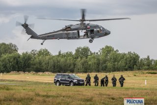 Policyjni kontrterroryści prowadzą skutego mężczyznę, który podróżował zatrzymanym SUV-em, nad nimi policyjny śmigłowiec.