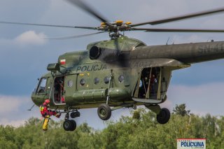 Zbliżenie na Mi-8 w locie, u jego burty zwisa na linie jeden ze strażaków.