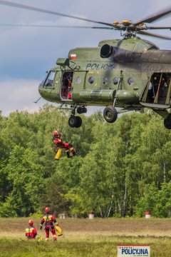 Strażak zjeżdża na linie ze śmigłowca Mi-8, w dole dwaj inni strażacy.