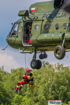 Zbliżenie na strażaka spuszczanego na linie z pokładu policyjnego Mi-8.