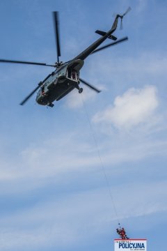 Strażacy zwisający na długiej linie pod kadłubem policyjnego Mi-8.
