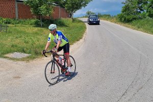 Rowerzysta zjeżdża ze wzniesienia i lekko skręca w prawo. Zanim samochód terenowy.