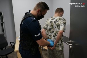 Umundurowany policjant zakłada kajdanki na ręce z tyłu zatrzymanemu mężczyźnie