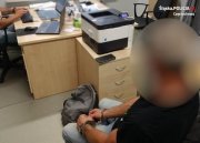 zatrzymany mężczyzna z kajdankami założonymi na ręce siedzi przed biurkiem policjanta&quot;&gt;