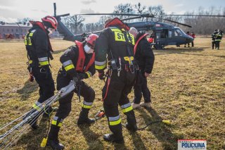 Na lądowisku grupa strażaków przygotowuje podłączenie haka Bambi Bucket do liny śmigłowca.