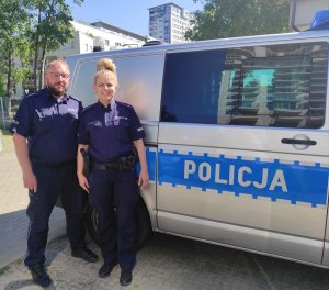 policjant i policjantka stoją przy radiowozie