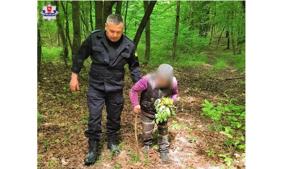 policjant wyprowadza z lasu zaginioną starszą panią