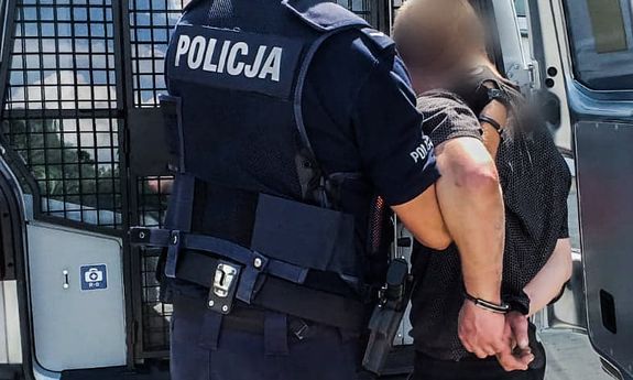policjant trzyma zatrzymanego mężczyznę, w tle tył radiowozu