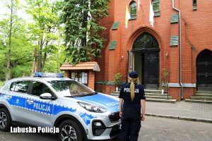 policjantka stoi przy radiowozie zaparkowanym przy kościele