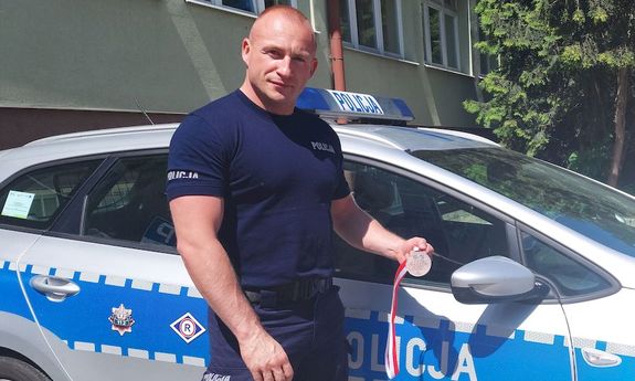 policjant, który brał udział w zawodach, stoi przy radiowozie i w ręku trzyma medal