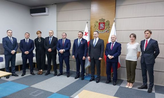 Dziesięcioro uczestników uroczystości, w tym dwie kobiety, pozuje do zdjęcia w siedzibie Ministerstwa Spraw Wewnętrznych Republiki Gruzji, z tyłu widoczne są flagi Polski i Gruzji