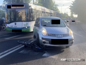 Pojazd osobowy stojący na przejściu dla pieszych, pod nim rower. W tle autobus miejski