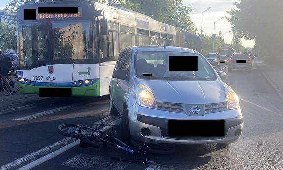 Pojazd osobowy stojący na przejściu dla pieszych, pod nim rower. W tle autobus miejski