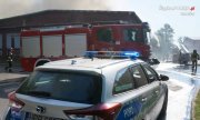 zdjęcie z miejsca pożaru, na pierwszym planie widać policyjny radiowóz i wóz strażacki, w tle dym nad budynkiem