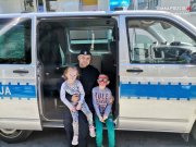 Zdjęcie przedstawiające policjanta z dziećmi w otwartych drzwiach policyjnego furgonu