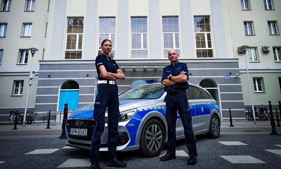 Umundurowani policjanci stoją przed radiowozem