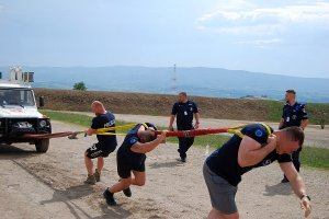 Trzech polskich policjantów ciągnie samochód za pomocą liny od lewej do prawej. Na twarzach widać duży wysiłek.