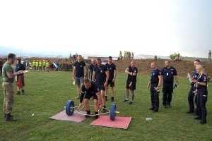 Policjant podnosi szkielet z rur, na którym założone są po obu stronach obciążniki. Cała konstrukcja waży 100 kilogramów.