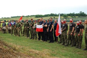 Uczestnicy zawodów w strojach sportowych i służbowych stają w dwuszeregu. Niektórzy mają pomalowane na biało-czerwono twarze. Polscy policjanci są w czarnych koszulkach.